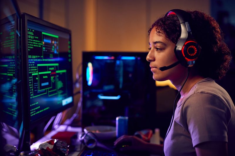 Female Teenage Hacker Sitting In Front Of Computer Screens Bypassing Cyber Security