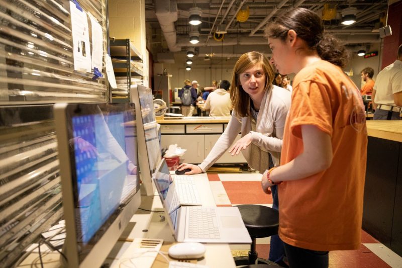 Two female students work in an open lab space on two computers.