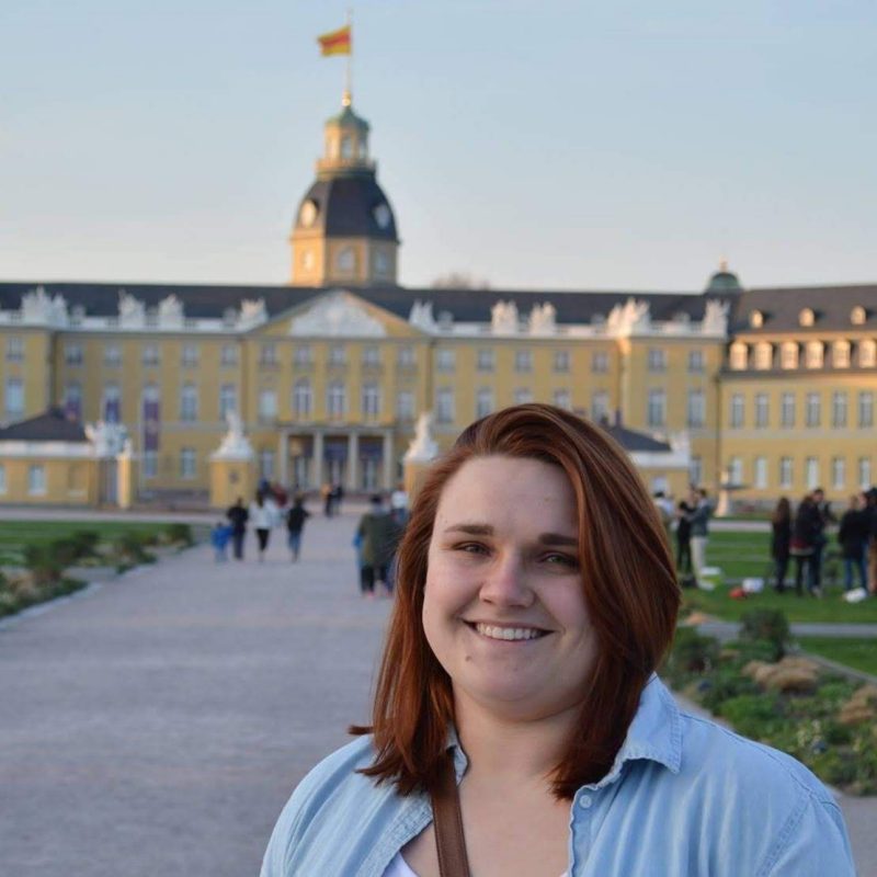 Young woman with red hair standing before a baroque palace
