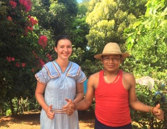 Young man and woman smiling in front of lush trees