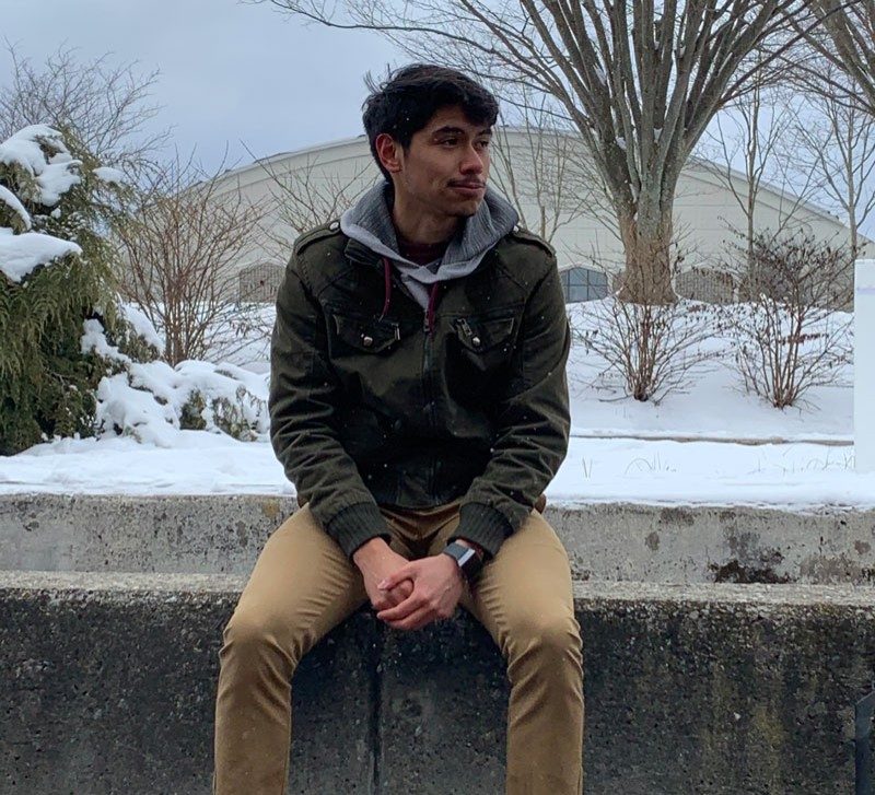 Christopher Lopez sitting on the wall in the snow with Cassell in the background.