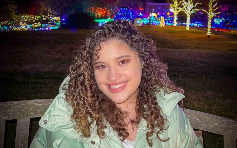 Valeria Lebron Berrios is sitting on a bench in front of Christmas lights