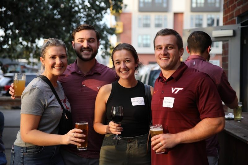 Four alumni smile for a photo with peer in their hand