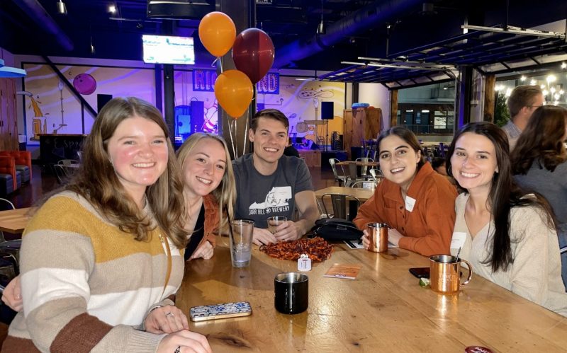 Five alumni sit around a table smiling