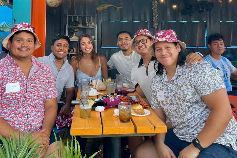 Six alumni sit around an outdoor table wearing Hawaiian shirts