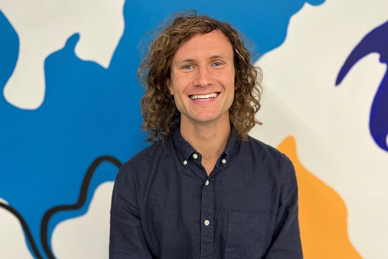 David Mackanic poses in front of a colorful mural 