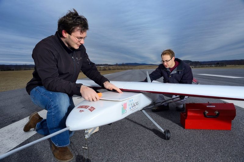 Students prepare a model plane for flight on an airstrip.