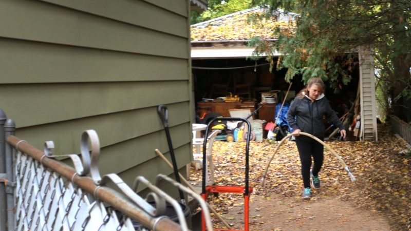 Keri Webber, Flint Michigan resident walking from her garage toward the front of the house with a plastic pipe