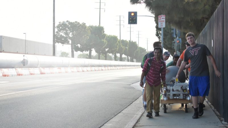 Several members of the Hyperloop team are pulling and pushing along a pod on the sidewalk.