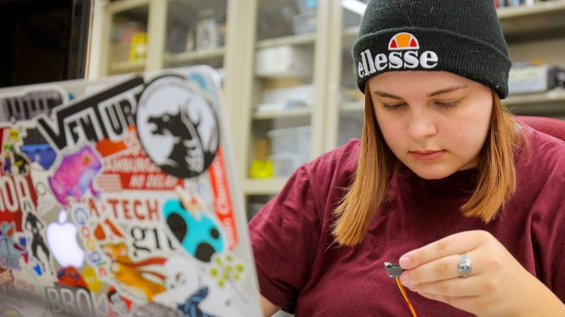 A student working with a laptop and a wire.