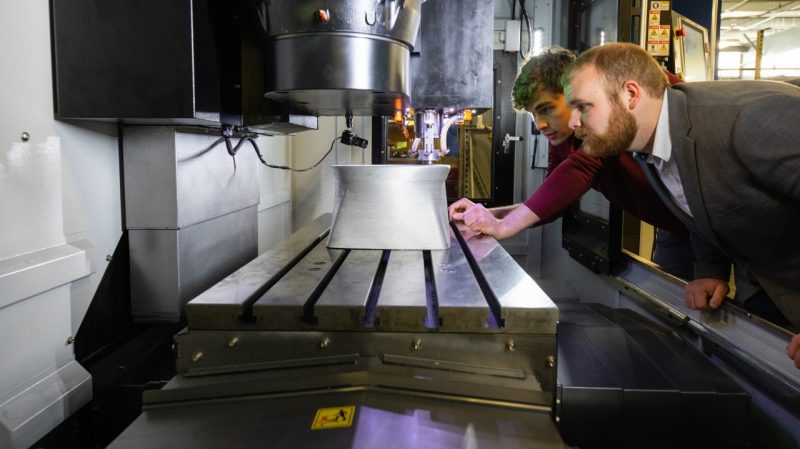 Student researchers look in at a 3D metal printer.