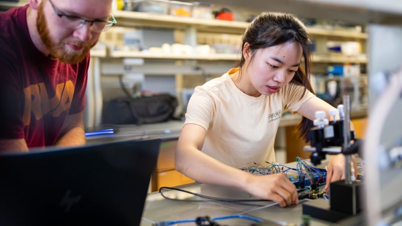 Two students working with equipment in a lab.