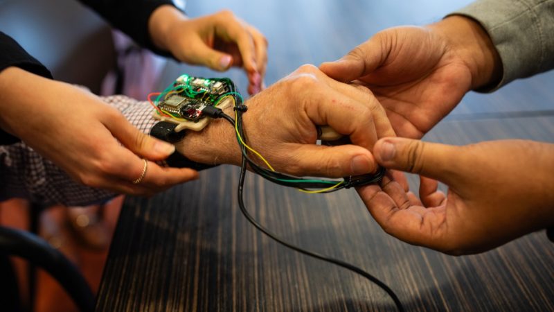 Two sets of hands help put on the wearable haptic wrist unit.