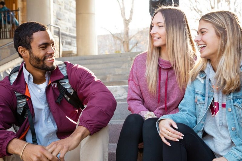 Group of students laughing while sitting on stairs outside of Pamplin Hall.